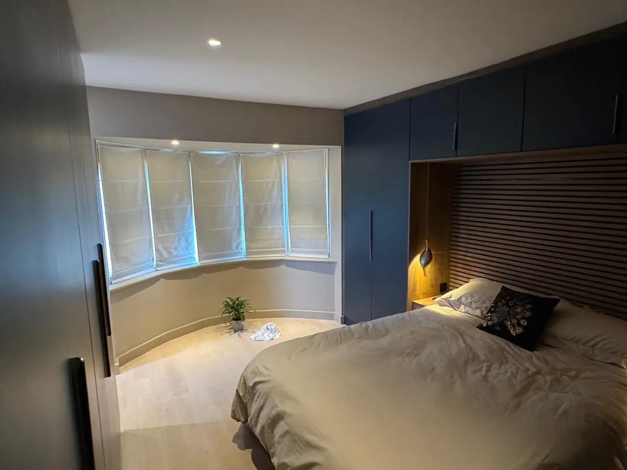 Navy fitted bedroom furniture beside a bay window with an oak headboard