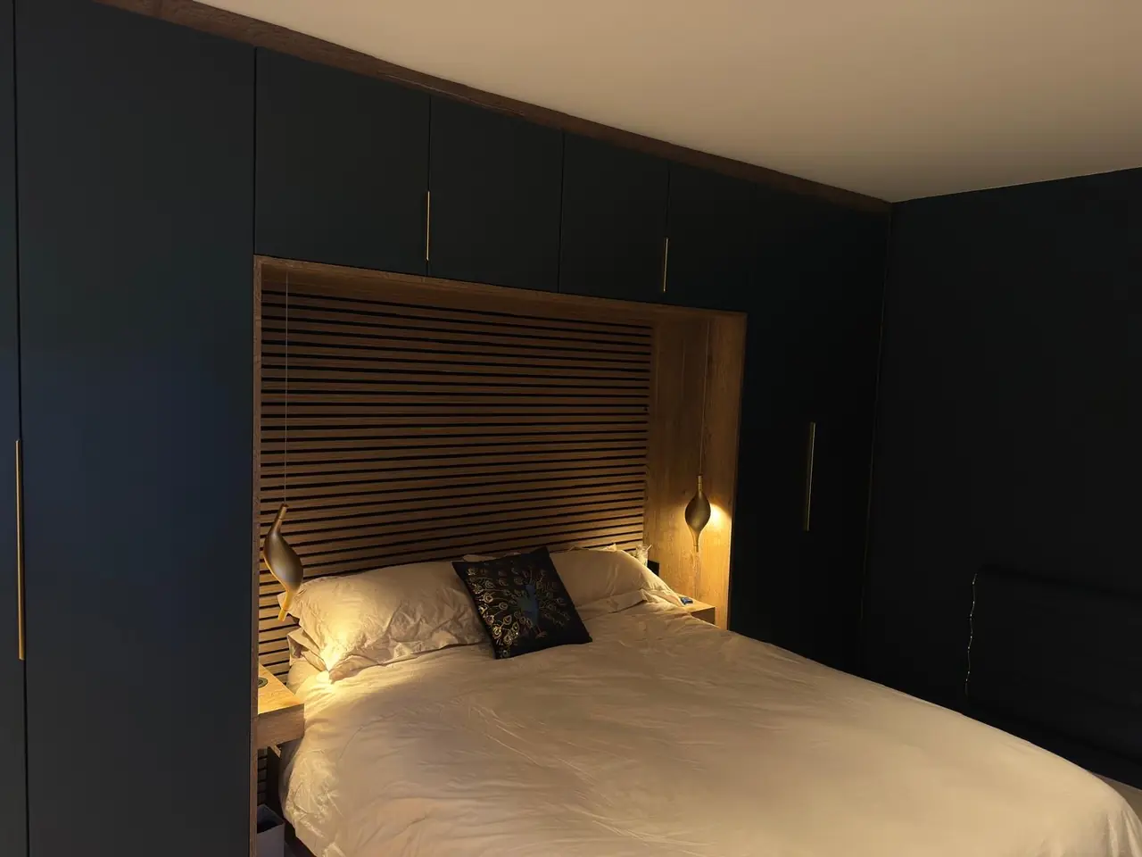 Navy fitted wardrobes either side of a bed nook with a slatted oak headboard