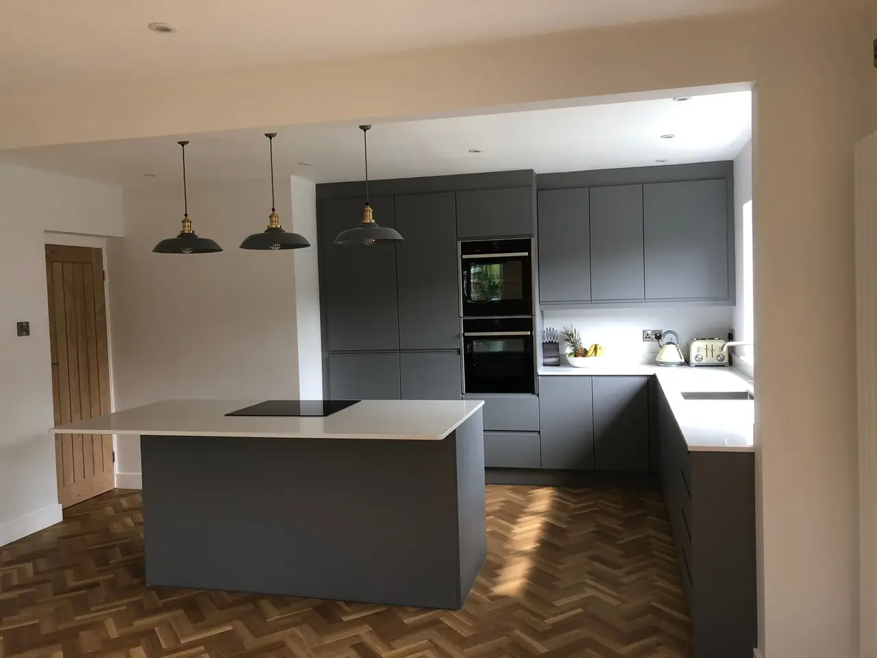 Anthracite kitchen with herringbone wood floor and pendant lights over the island