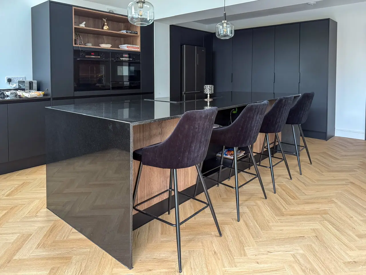 Black kitchen with an oak-topped island, bar stools and herringbone floor