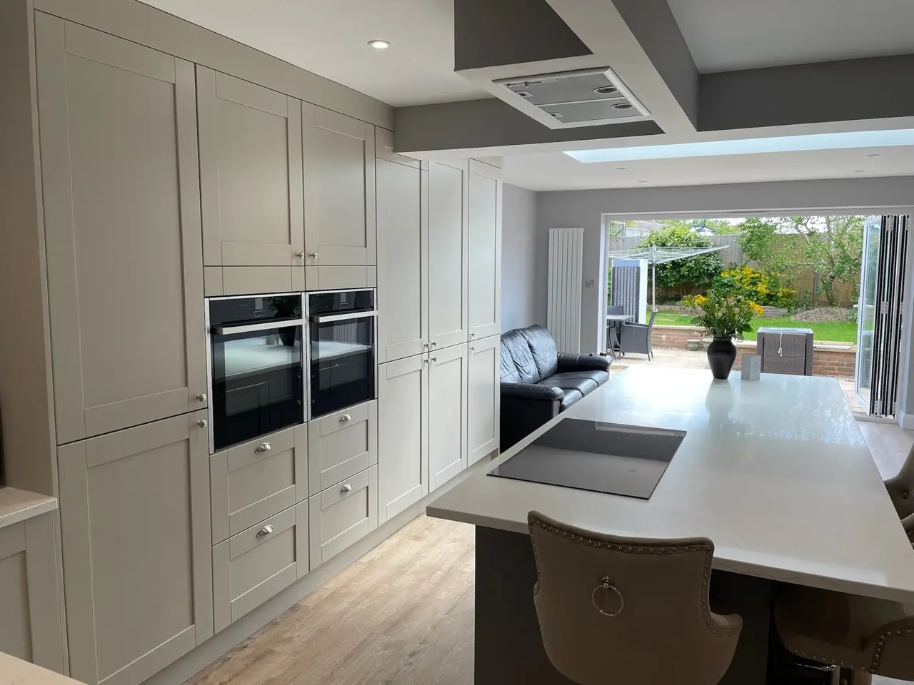 Taupe shaker kitchen with double ovens and bifold doors to the garden