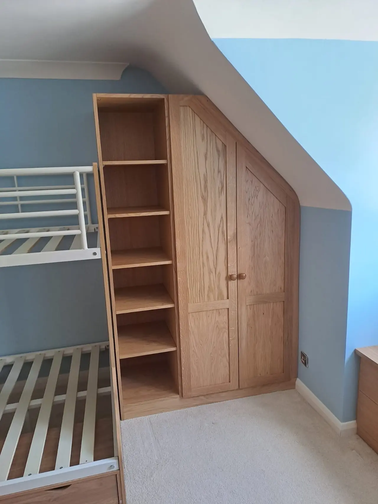 Oak wardrobes built into a sloping ceiling in a bunk room