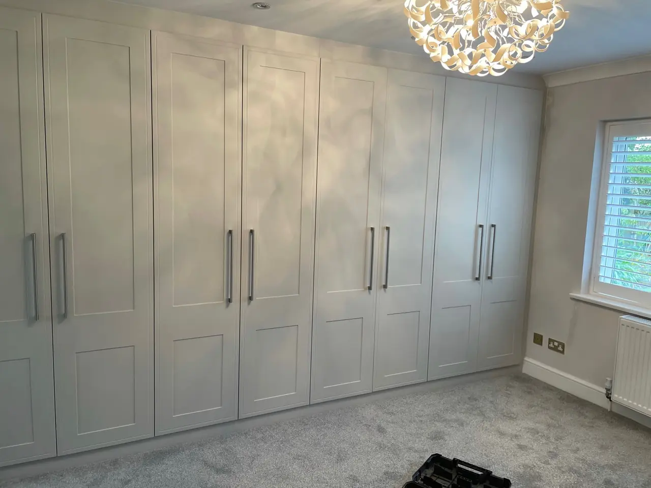 Light grey shaker wardrobes with hinged doors below a chandelier