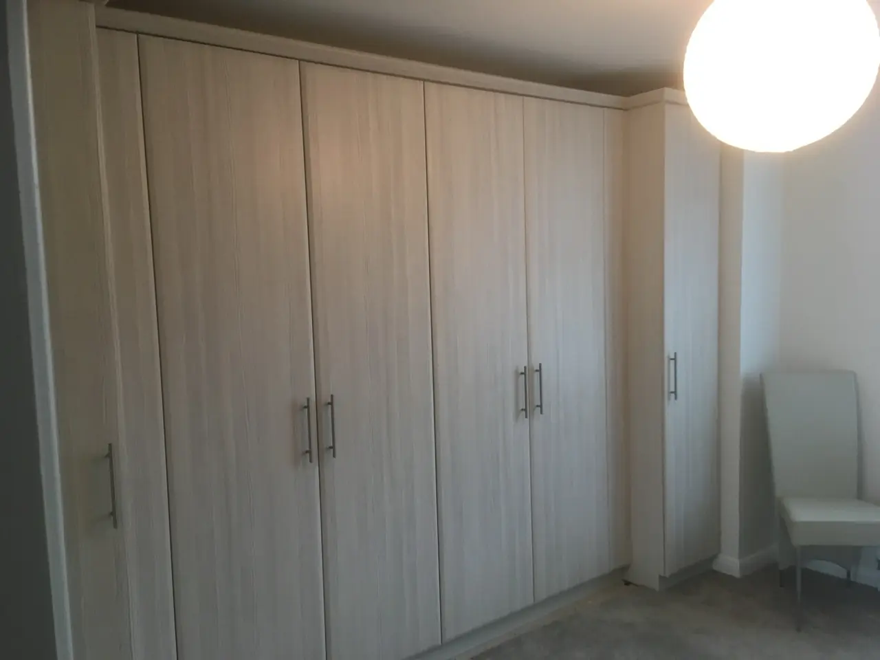 Fitted oak wardrobes with hinged doors running the length of a bedroom wall